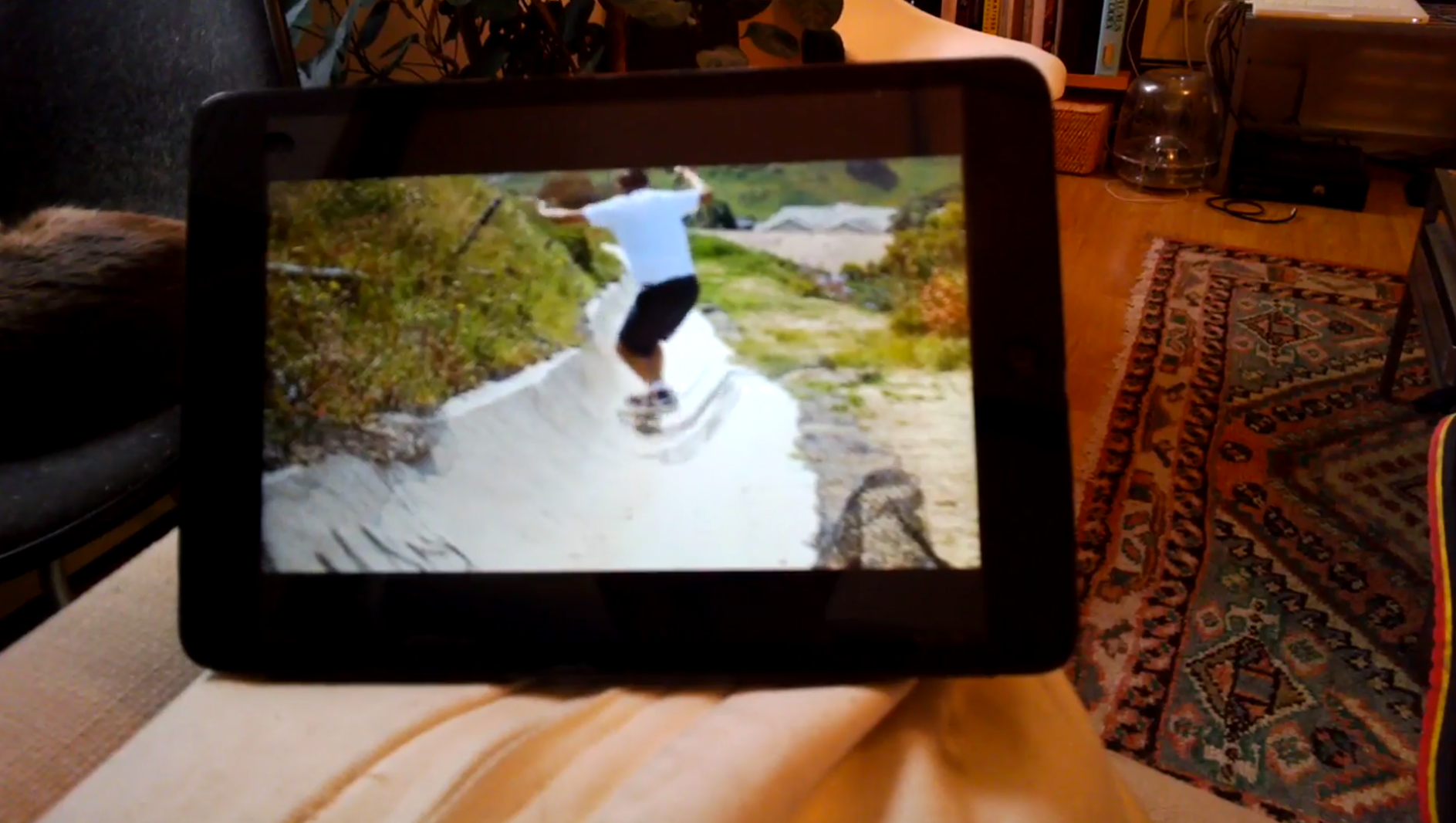 a still from Trevor Shimizu's lonely loser trilogy: skate videos - a man sits on the living room couch holding an ipad, watching skate videos. the image is taken POV style from the protagonist's google glasses.