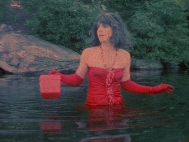 A white woman with brown hair wades in blue water wearing a red dress.